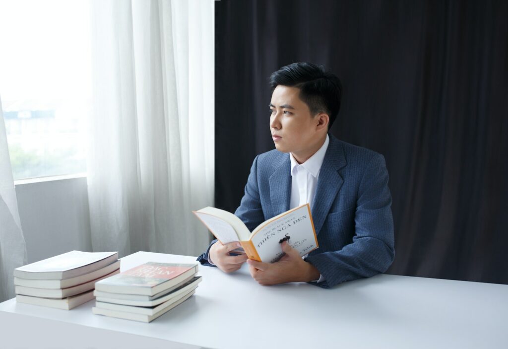 Photo of a Pensive Young Man in a Suit Holding a Book